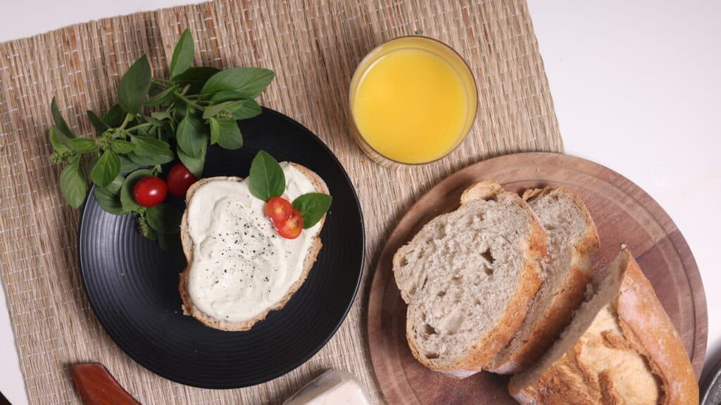 Queijo vegano com manjericão e tomate fresco, pão artesanal e suco de laranja natural.