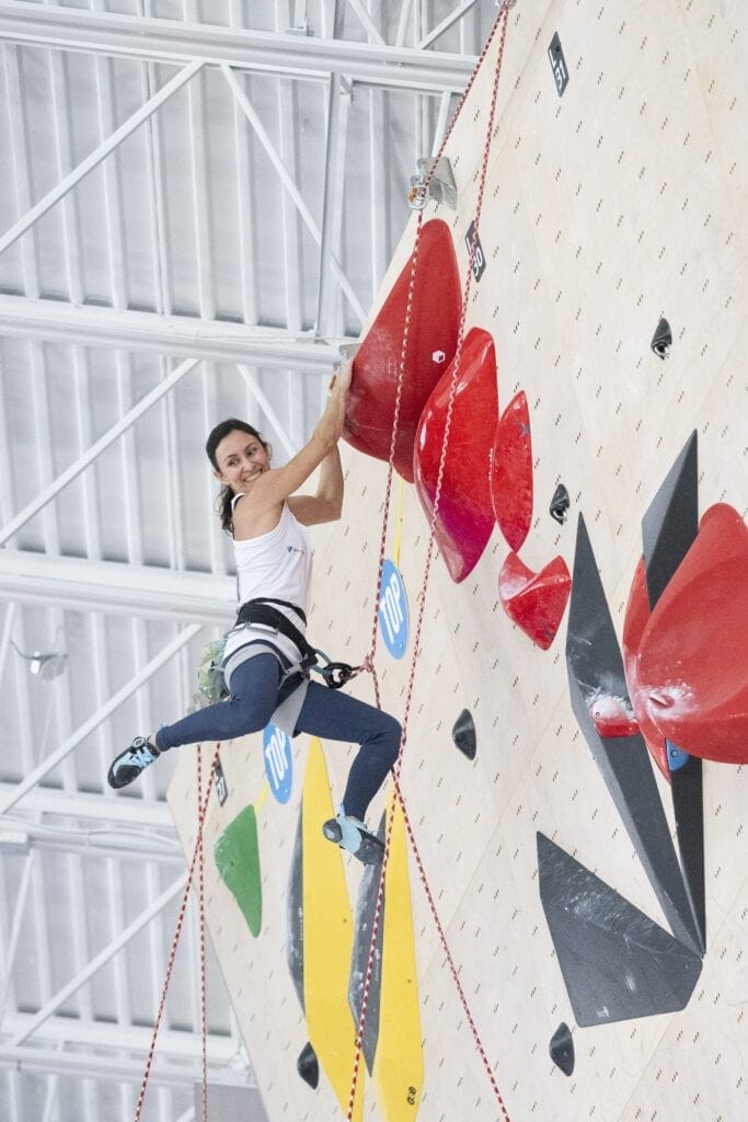Pavimentação de rocha artificial para escalada indoor com atleta usando equipamento de segurança.