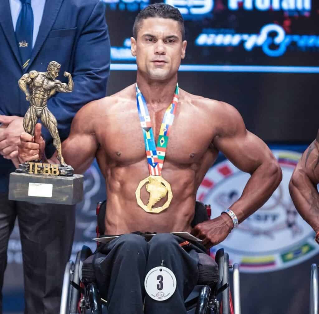Atleta paralímpico com medalha no peito e troféu em mãos, conquistando vitória em campeonato internacional.