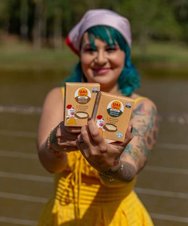 Tofu vegano UAI Tofu com embalagem em destaque, mulher sorridente ao ar livre, promove produtos artesanais e saudáveis.